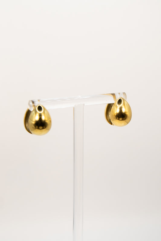 Gold teardrop earrings on a clear stand against a white background