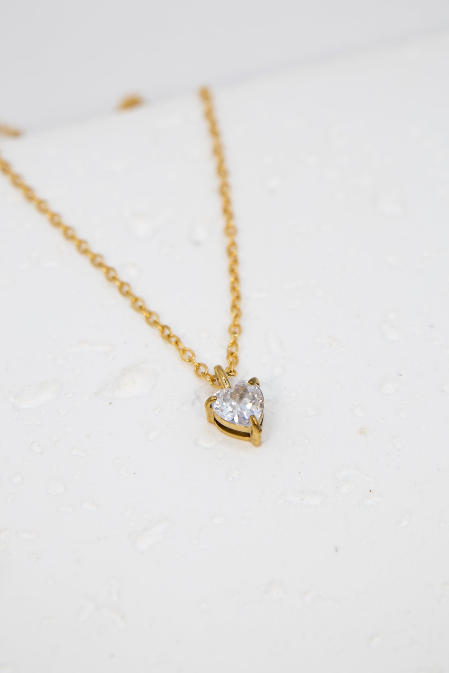 Gold necklace with a heart-shaped diamond pendant on a white background