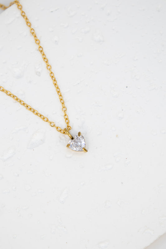 Gold necklace with a heart-shaped diamond pendant on a white background