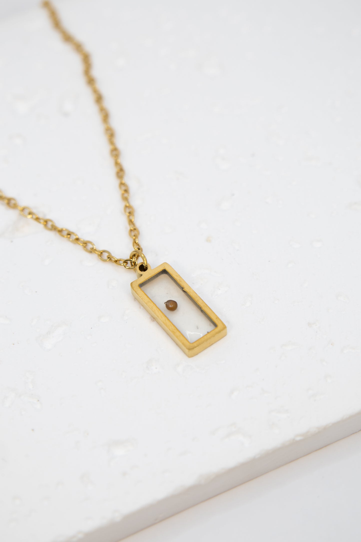 Gold necklace with a rectangular pendant on a white background