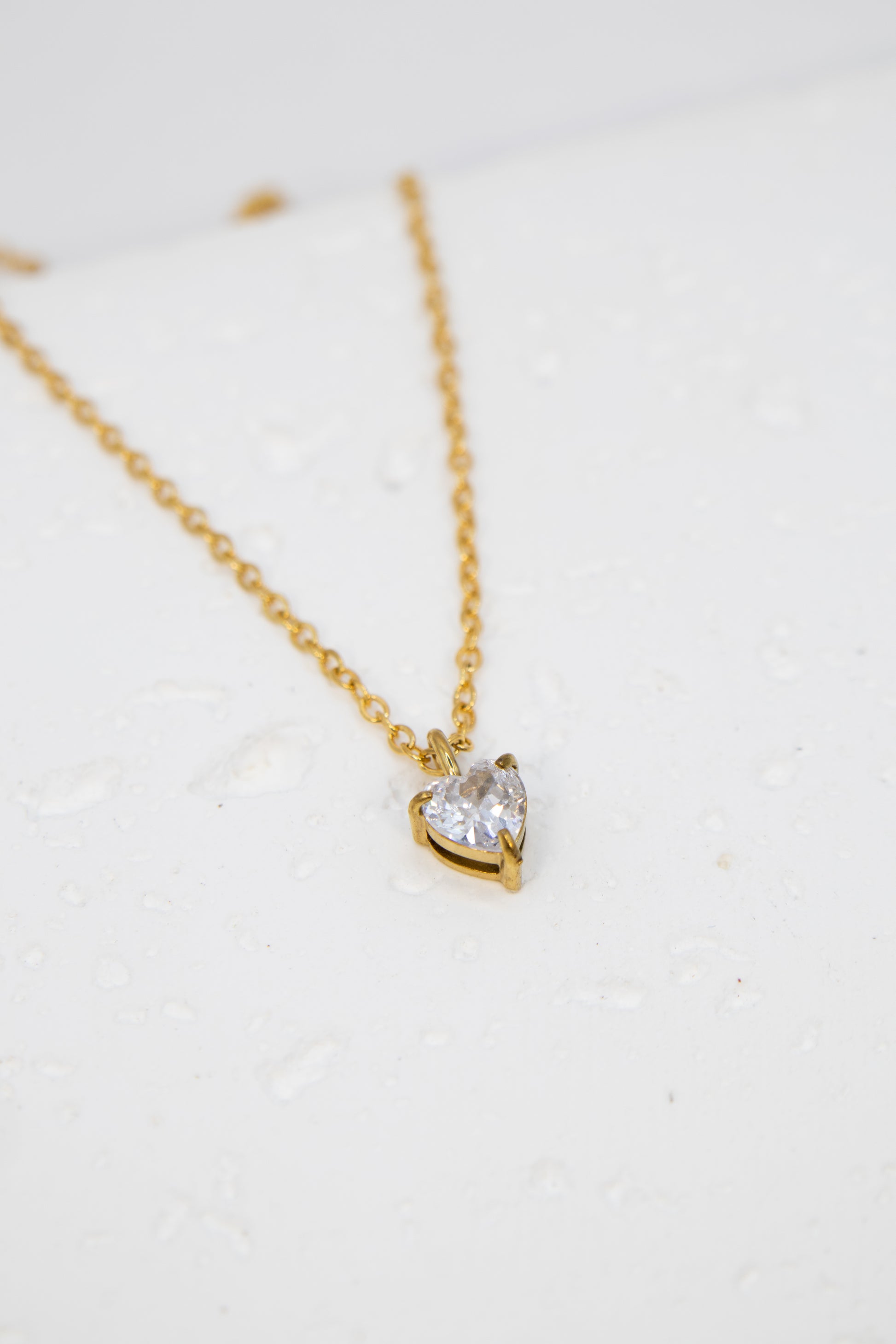 Gold necklace with a heart-shaped diamond pendant on a white background
