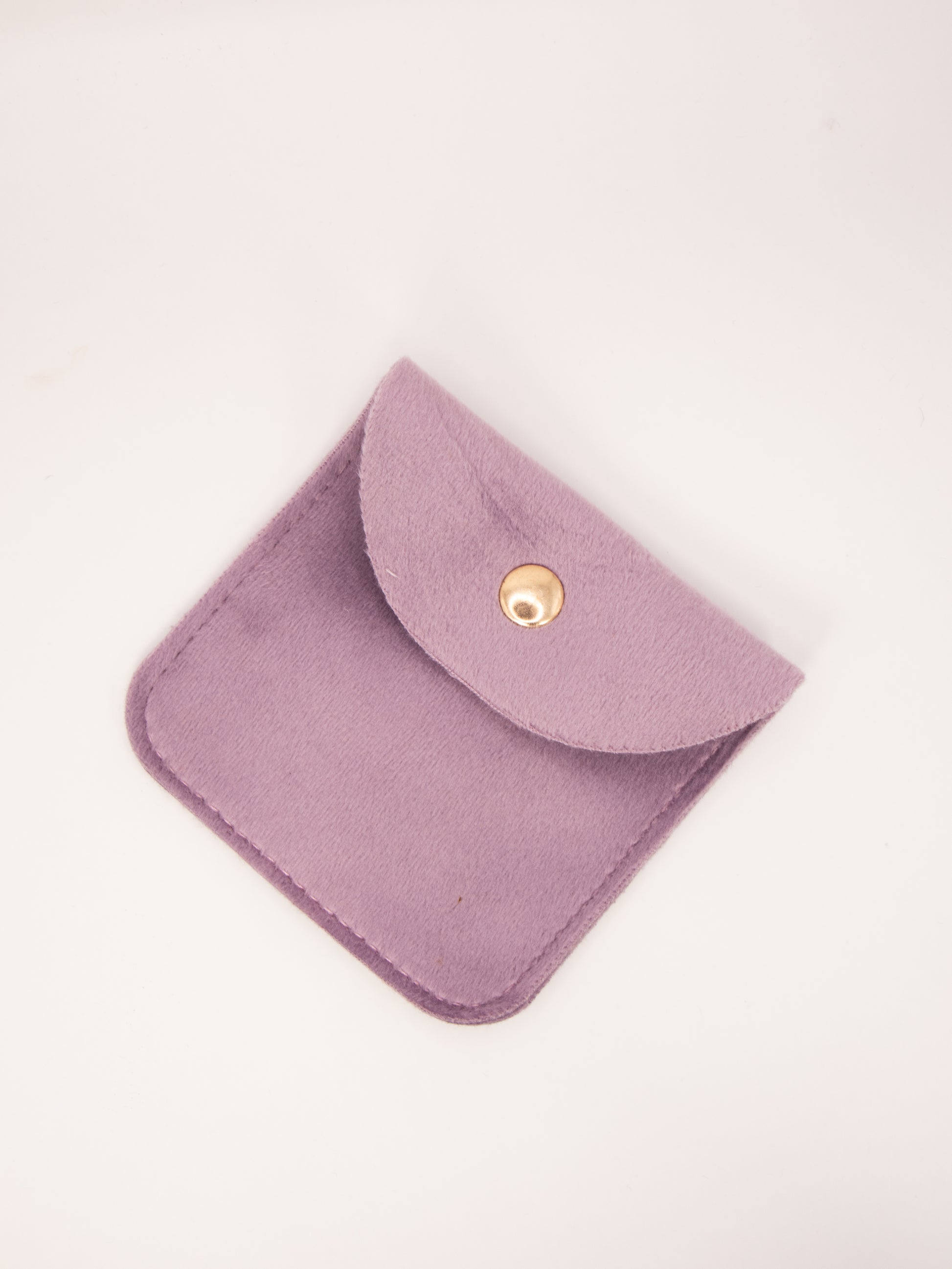 Purple fabric pouch with a gold button on a light pink background