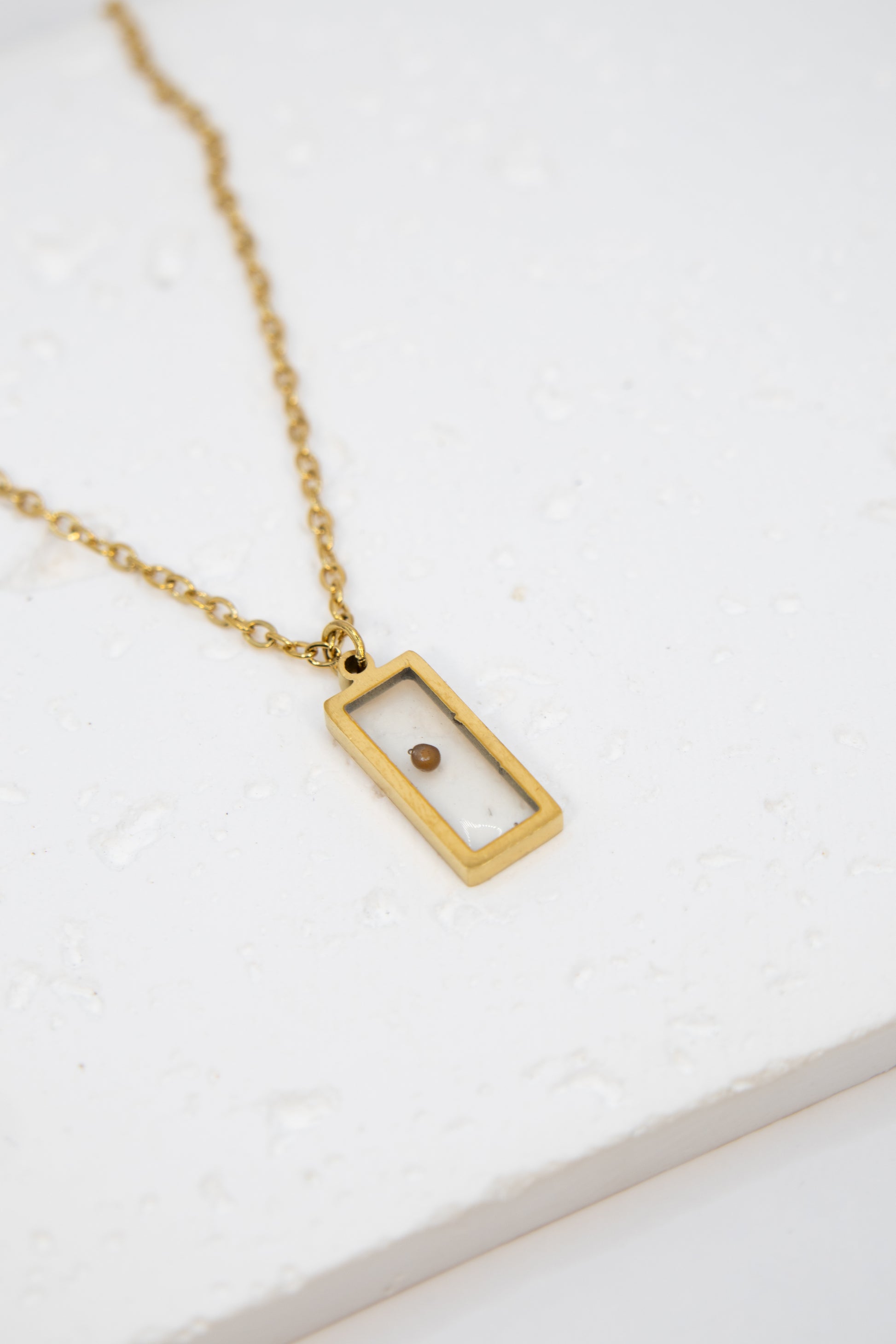 Gold necklace with a rectangular pendant on a white background