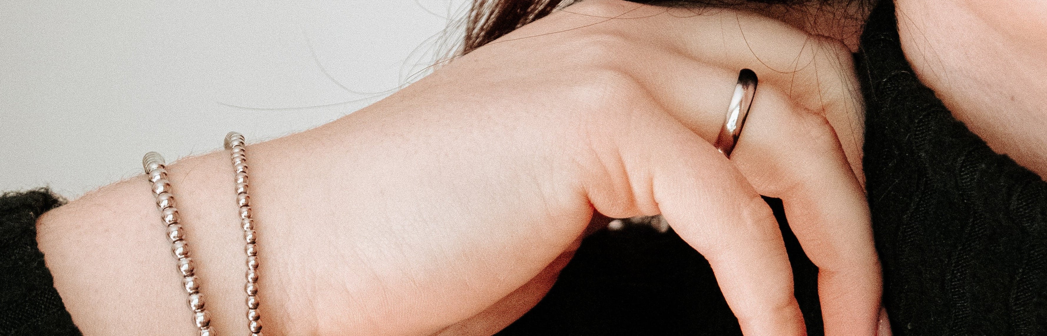Close-up of a person wearing hoop earrings, a ring, and bracelets on a plain background