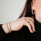 Close-up of a person wearing hoop earrings, a ring, and bracelets on a plain background