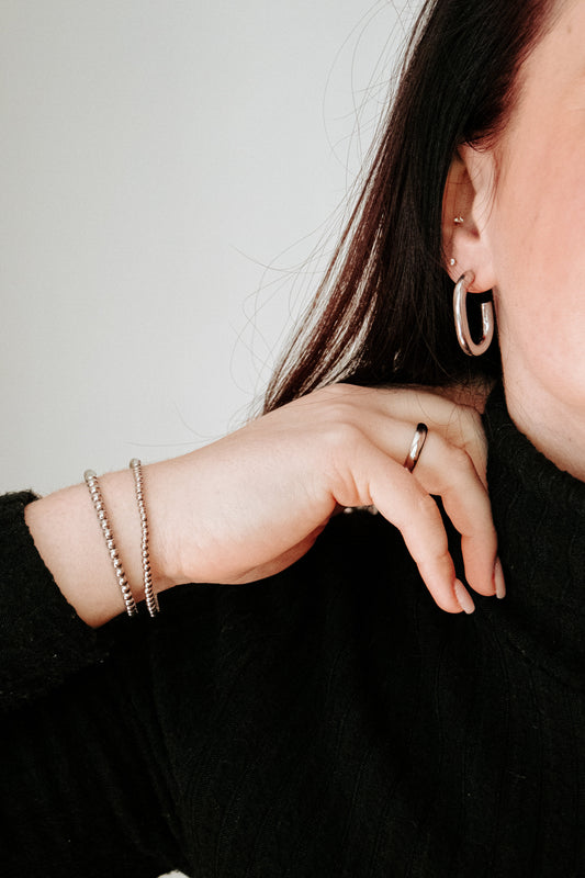 Close-up of a person wearing hoop earrings, a ring, and bracelets on a plain background